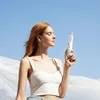 A young woman holds a portable fan against a bright blue sky. Produktbild-Vorschau