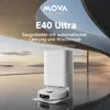 A white robot vacuum cleaner and its charging station are displayed in front of a large window with a scenic view of mountains and water. Produktbild-Vorschau