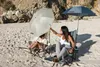 Two people sitting on chairs on a sandy beach under umbrellas. Produktbild-Vorschau