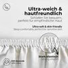 Close-up of a white fabric with text overlays highlighting product features like softness, skin-friendliness, and elasticity. A detail of the elasticated edge is magnified. Produktbild-Vorschau