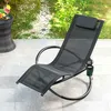 A black rocking lounge chair with a headrest and cup holder sits on a paved patio next to a small table with a drink and fruit. Anteprima dell’immagine prodotto