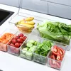 A clear plastic organizer filled with various fruits and vegetables, including bananas, lettuce, carrots, tomatoes, and cucumbers, arranged on a countertop. Produktbild-Vorschau