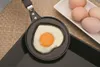 A heart-shaped fried egg in a mini-pan, with raw eggs in the background. Podgląd zdjęcia produktu