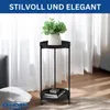 A black metal plant stand with two shelves, holding a potted plant on the top shelf and books on the bottom shelf, in a room with sheer white curtains and sunlight filtering through. Podgląd zdjęcia produktu