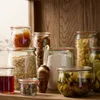 A collection of glass jars filled with various food items and a copper scoop on a wooden shelf. Anteprima dell’immagine prodotto