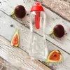 A clear plastic water bottle with a red lid and internal filter, surrounded by fresh figs on a wooden surface. Anteprima dell’immagine prodotto