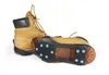 A pair of tan boots with black accents, one boot is upright and the other is lying on its side showing the sole with blue snowflake-like traction grips. Produktbild-Vorschau