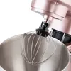 A close-up view of a rose gold stand mixer's whisk attachment and mixing bowl. Podgląd zdjęcia produktu