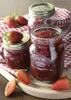 Three jars of strawberry jam are arranged on a wooden board with fresh strawberries and a red and white checkered cloth. Voir les images du produit