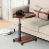 A mobile C-table with a camera and phone on top, placed next to a sofa with a decorative pillow. A robot vacuum cleaner is visible on the floor. Produktbild-Vorschau