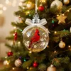 A close-up of a Christmas tree ornament shaped like a clear glass ball with a red cardinal inside, hanging on a decorated Christmas tree. Produktbild-Vorschau