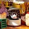 A close-up view of a miniature kitchen scene, featuring a kettle on a stove, a basket with food, and decorative elements. Podgląd zdjęcia produktu