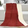 A red and beige blanket draped over a sofa. Náhled obrázku produktu