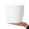 A hand holding a white plant pot with a saucer. Náhled obrázku produktu