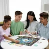 Four young people are playing a board game at a round table. Produktbild-Vorschau