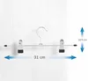 A metallic hanger with two clips for hanging pants or skirts, shown against a white wooden background with dimension labels. Produktbild-Vorschau