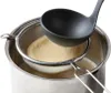 A ladle is used to strain a beige-colored mixture into a metal pot through a mesh sieve. Anteprima dell’immagine prodotto