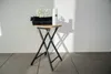 A white spray bottle and black towels are placed on a wooden stool against a white wall. Produktbild-Vorschau