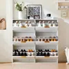 A white shoe cabinet with multiple drawers is filled with shoes. A plant and framed art are on top of the cabinet. Produktbild-Vorschau