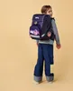 A young girl wearing a backpack and jeans, looking over her shoulder. Produktbild-Vorschau