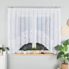 A white lace curtain is displayed in front of a window, with plants and decorative items on the windowsill. Produktbild-Vorschau
