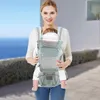 A woman is carrying a baby in a carrier outdoors with a body of water and a building in the background. Náhled obrázku produktu