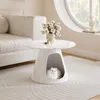 A white coffee table with a built-in pet bed is placed on a light gray rug in a living room setting. A vase of white flowers sits on top of the table. Produktbild-Vorschau