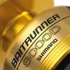 A close-up of a gold fishing reel with text indicating the brand and model. Anteprima dell’immagine prodotto