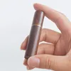 A hand holds a small, cylindrical wooden object with a gold band around its middle. Produktbild-Vorschau
