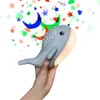 A hand holding a whale-shaped night light with colorful stars and moons projected above it. Produktbild-Vorschau