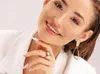 A close-up portrait of a woman wearing a white blazer, smiling and touching her chin. She has long, light pink nails and is wearing jewelry. Anteprima dell’immagine prodotto