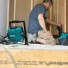 A person is working on plumbing in a construction setting, with a work light nearby. Podgląd zdjęcia produktu