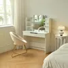 A white vanity table with a lighted mirror, a beige chair, and a bedside table with a lamp in a bedroom. Produktbild-Vorschau