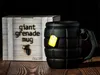 A black grenade-shaped mug with a yellow tea bag tag is placed next to its packaging box on a wooden surface. Voir les images du produit