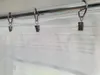 A close-up view of a white sheer curtain hanging from a metal rod with clip rings. Produktbild-Vorschau