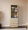 A tall, narrow storage unit with shelves and drawers, filled with folded clothes, stands against a plain wall. A vase with dried reeds is to the left. Produktbild-Vorschau