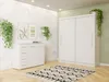 A white wardrobe and chest of drawers are shown in a room with plants and artwork. Náhled obrázku produktu