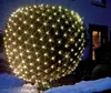 A spherical bush decorated with a net of warm white LED lights, set against a dark background with a house and snow in the foreground. Produktbild-Vorschau