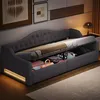 A gray upholstered daybed with storage drawers is shown in a bedroom setting, with the mattress partially lifted to reveal the storage compartment. Anteprima dell’immagine prodotto