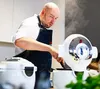 A man in a chef's apron is cooking with a modern kitchen appliance that is emitting steam. Podgląd zdjęcia produktu