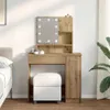 A vanity table with a mirror and lights, a stool, and a plant in a room. Náhled obrázku produktu