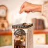 A hand is placing a clear panel on top of a miniature book nook. Podgląd zdjęcia produktu