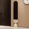 A tall, oval-shaped mirror with a rounded base stands next to a dark brown door. A clock is visible on the wall in the background. Produktbild-Vorschau