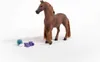 A brown toy horse with a braided mane and tail stands on a white surface next to grooming accessories. Voir les images du produit