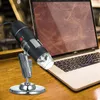 A digital microscope is shown on a stand, placed on a wooden desk next to a laptop. Podgląd zdjęcia produktu