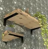 Two wooden shelves with black brackets mounted on a wall with a dandelion pattern wallpaper. A plant is on the top shelf, and a pot with a plant is on the bottom shelf. Produktbild-Vorschau
