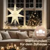 A festive Christmas scene with a star lamp and a decorated Christmas tree in a window, with a couch and candles in the foreground. Produktbild-Vorschau