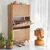 A wooden shoe cabinet with rattan detailing is shown in a room with plants and a stool. Produktbild-Vorschau