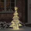 A lighted Christmas tree decoration stands outside a brick building next to a window. Podgląd zdjęcia produktu