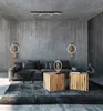 A modern living room with a grey concrete wall, a sectional sofa, two wooden cube tables, and a large dark rug. Voir les images du produit